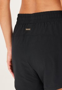 Zwarte sportshorts met een elastische tailleband. Kenmerkt zich door een klein metalen logo aan de achterkant, een gladde stof en een eenvoudig ontwerp.