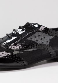 Chaussures noires à lacets combinant cuir verni brillant et mesh avec des accents à pois et une surface texturée.