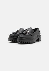 Mustad nahast loafers, millel on robustne, tekstureeritud tald, dekoratiivsete tutti ja kuldse värvusega vööpinna aksessuaariaktsent.