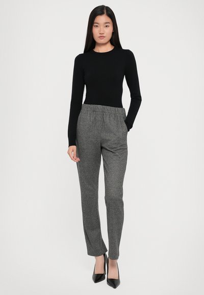 Schwarzes Langarmshirt kombiniert mit grauen, strukturierten, elastischen Hosen mit Bund. Schwarze spitze Absätze runden das Outfit ab.