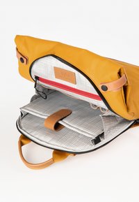 Gelbe Lederhandtasche mit einem oberen Klappdeckel, ausgestattet mit einem grau karierter Innenausstattung, einer roten Reißverschlusstasche und einem braunen Lederakzentriemen.