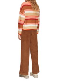 Gehaakte gestreepte trui in rood, beige en roze; losse pasvorm. Gecombineerd met een bruine corduroy broek met wijde pijpen. Chunky beige schoenen.