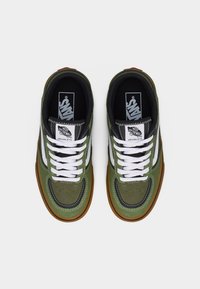 Ζευγάρι από πράσινα και μαύρα sneakers Vans Rowley με λευκά κορδόνια και σόλες σε χρώμα καραμέλας, από πάνω σε λευκό φόντο.