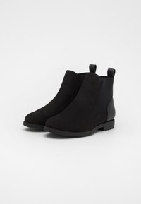 Black ankle boots made of suede and elastic material, featuring a round toe, low heel, and pull tabs for easy wear.