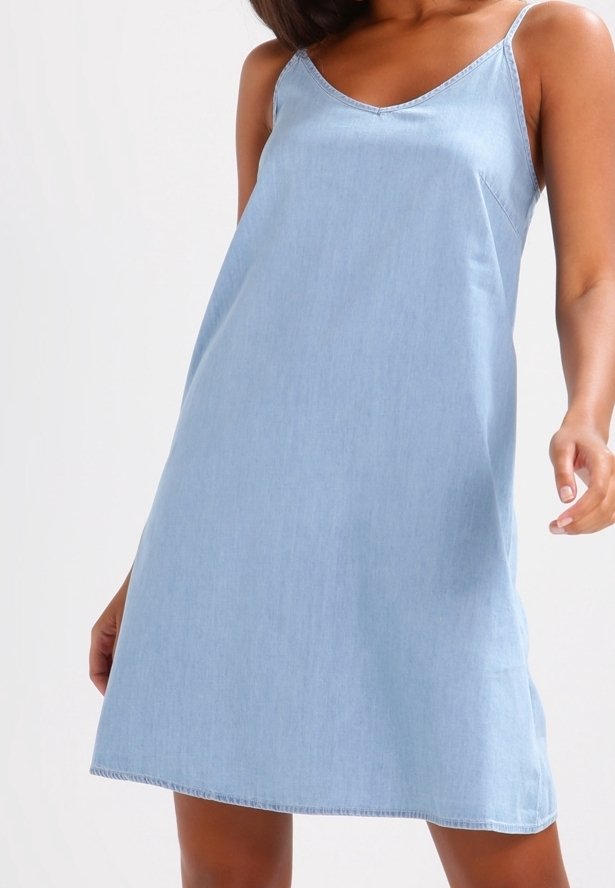 Robe en denim bleu clair sans manches avec une coupe décontractée. Elle présente un col en V, des bretelles fines et un détail de couture minimal le long des bords.