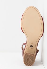 Semelle d'une sandale rouge pour femme montrant un dessous beige lisse, talon texturé marqué "ANTI SLIDE," taille 37, et nom de marque "Tamaris."