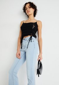 Svart heklet topp med knyte-detaljer og sølvkjede-stropper, parret med lyseblå flared jeans og en liten svart håndveske.