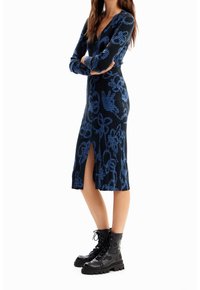 Sukienka dzianinowa w kolorze czarnym z niebieskim wzorem kwiatowym, z długimi rękawami, głębokim dekoltem w serek, o długości do połowy łydki oraz z rozcięciem po boku. Połączona z czarnymi butami wojskowymi.
