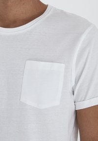 T-shirt bianco a maniche corte realizzato in tessuto leggero, dotato di taschino sul petto e orli arrotolati. Tessuto liscio con dettagli di cuciture sottili.