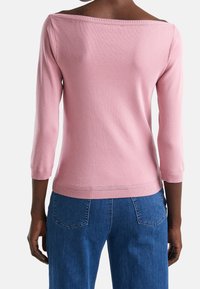 Pink knit sweater with a wide neckline and three-quarter sleeves, featuring a ribbed hem and cuffs, paired with blue denim jeans.
