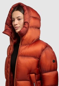 Kurtka puchowa w intensywnym pomarańczowym kolorze z teksturowanym, błyszczącym wykończeniem. Posiada wysoki kołnierz, oversize'owy kaptur oraz zapięcie na zamek z przodu.