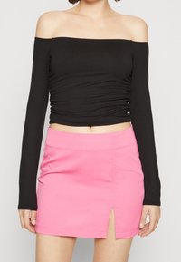 Svart av axeln långärmad topp som matchar med en rosa minikjol med sidöppning, tillverkad av stretchigt tyg med en mjuk textur.