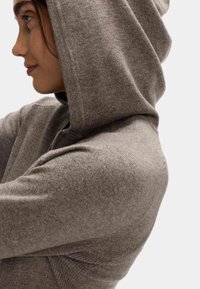Šedá mikina na zip s texturovaným materiálem, vybavená kapucí a žebrovanými detaily na ramenou a manžetách. Měkký, volný střih.