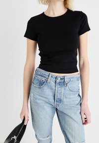 Svart kortärmad t-shirt med rund halsringning, kombinerad med ljusblå slitna jeans. Texturerat tyg, avslappnad passform.