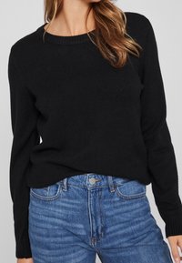 Czarny sweter z dzianiny o okrągłym dekolcie, z długimi rękawami i ściągaczami, zestawiony z jasnoniebieskimi dżinsami o klasycznym kroju.