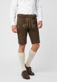Lederhosen marroni con ricami floreali, piping dorato e tasche laterali; abbinati a calze crema fino al ginocchio e scarpe marroni.