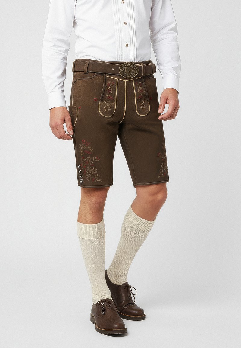 Lederhosen marroni con ricami floreali, piping dorato e tasche laterali; abbinati a calze crema fino al ginocchio e scarpe marroni.