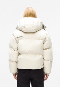 Pufferjack in lichtbeige met een hoge kraag, met gestikte delen en elastische manchetten. Merknamen "KARL LAGERFELD" op de achterkant.