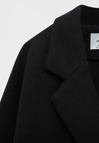 Cappotto in misto lana nera con colletto, caratterizzato da una finitura testurizzata e un design pulito. Etichetta visibile all'interno del colletto.