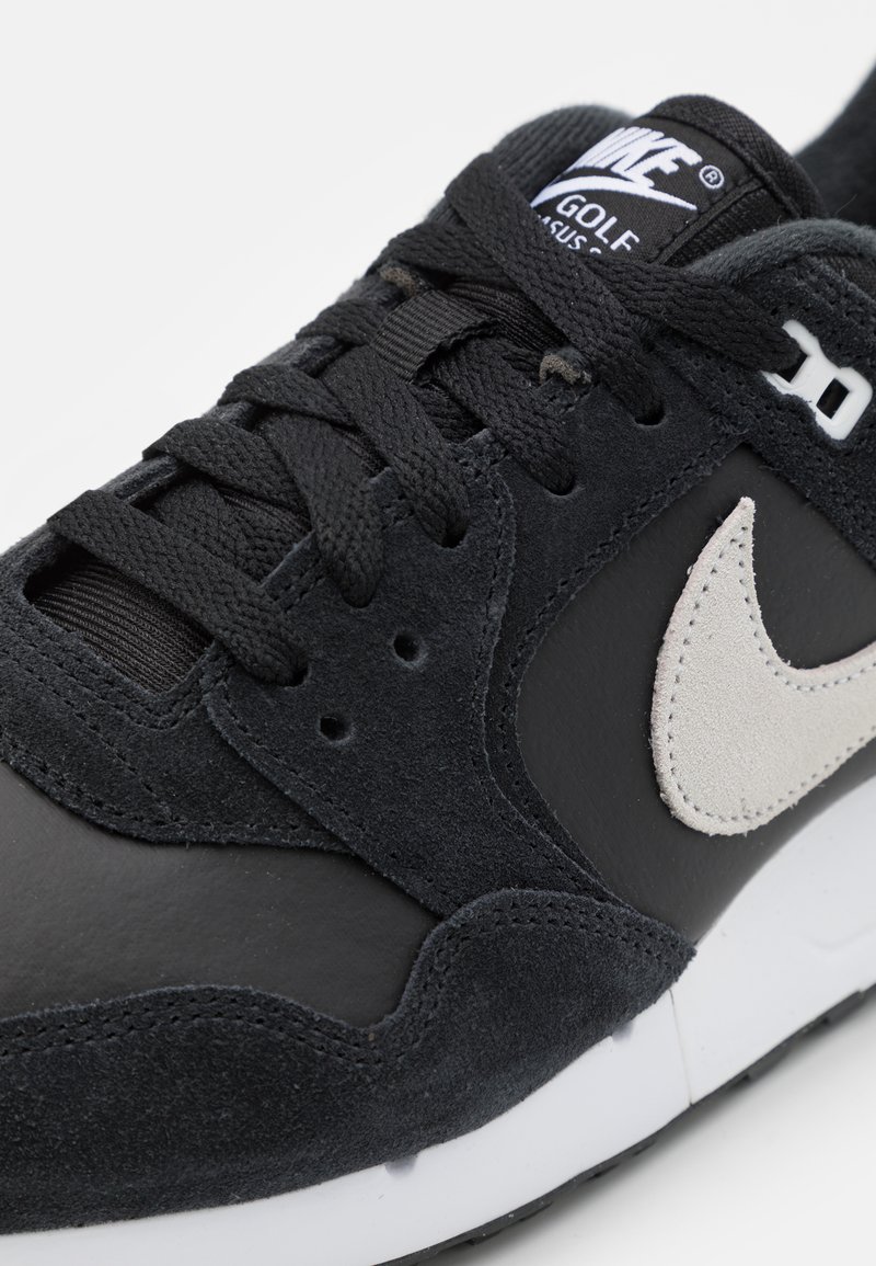 Schwarze Sneaker mit Wildleder- und Lederoberfläche, ausgestattet mit einem hellgrauen Nike-Swoosh, schwarzen Schnürsenkeln und einer weißen Zwischensohle.