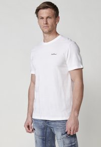 T-shirt bianco a maniche corte con strisce orizzontali testurizzate, con un piccolo logo nero sul petto. Vestibilità casual, collo tondo.