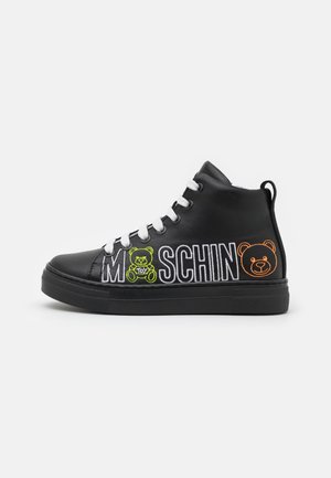 Zwarte hoge sneaker met witte veters, voorzien van de tekst "MOSCHINO" en een groene en oranje teddybeer borduring aan de zijkant.