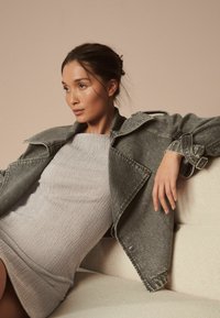 Gray denim jacket with wide collar and belted sleeves over a light ribbed dress. Soft fabric textures, neutral color palette, minimalist design.