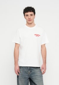 Bílé bavlněné tričko s krátkými rukávy a kulatým výstřihem, s červeným nápisem "FRUITS OF LOVE" na levé straně hrudi.