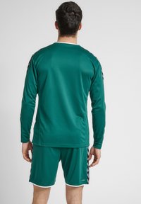 Grøn atletisk langærmet trøje med sorte skulderdetaljer og matchende shorts, der har en behagelig, glat tekstur og sporty design.