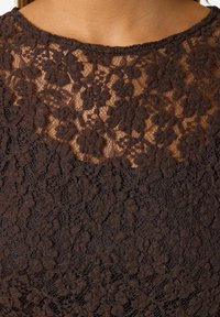 Tmavě hnědý krajkový top se květinovým vzorem, texturovaným povrchem a kulatým výstřihem, s propracovanými detaily podél okrajů.