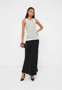 Siva top brez rokavov z belimi poudarki, kombinirana s črno maxi krilo. Črni visoki škornji in majhna črna torbica dopolnjujejo videz.