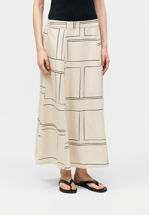 Pantalon beige à jambes larges avec motif de lignes géométriques noires, porté avec un haut sans manches noir et des sandales plates noires.