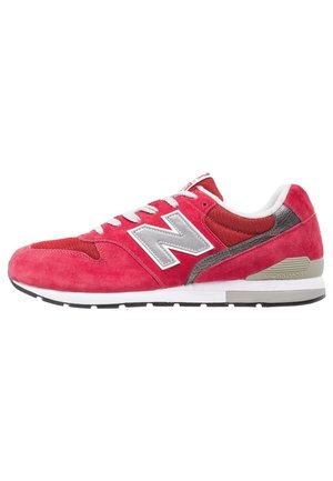 Rød New Balance-sneaker med hvide snørebånd, grå "N"-logo, grå og hvid sål samt overdele i ruskind og mesh.