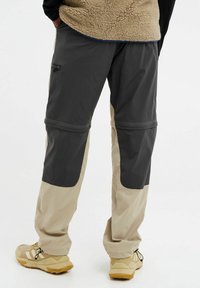 Heren outdoorbroeken in zwart en bruin, met een ritszak, contrasterende panelen en een elastische tailleband, vervaardigd uit lichtgewicht stof.