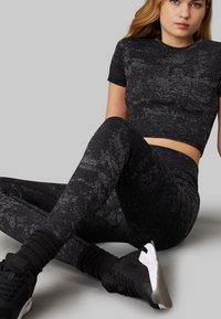 Completo sportivo nero composto da una maglietta cropped aderente a maniche corte e leggings a vita alta con un motivo testurizzato. A completare il look, sneakers nere.