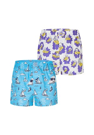Muskelbepackter Mann mit geflochtenem Haar und Kinnbart steht frontseitig und trägt hellblaue Boxershorts mit weißen Segelboot- und Wolkenmotiven.
