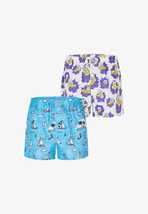 Muskelbepackter Mann mit geflochtenem Haar und Kinnbart steht frontseitig und trägt hellblaue Boxershorts mit weißen Segelboot- und Wolkenmotiven.