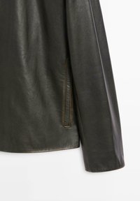 Dark green leather jacket with a smooth texture, featuring a side pocket and contrasting stitching. Simple design with a relaxed fit.