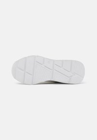 Suela de zapatilla de goma blanca con patrones texturizados, que presenta formas geométricas elevadas y ranuras para tracción, proporcionando estabilidad y agarre.