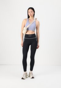 Light purple ribbed sports crop top, high-waisted black leggings with white accents, and a beige crossbody bag. Fashionable athletic look.