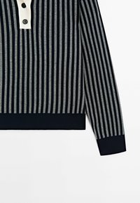 Navy and gray striped pullover with a contrasting cream button placket. Features ribbed cuffs and hem, made from soft fabric.