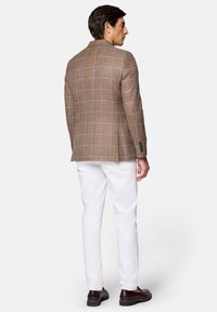 Brązowa marynarka w kratę z niebieskimi liniami, z klapami typu notch oraz guzikami na mankietach, zestawiona z białymi spodniami i ciemnymi butami.