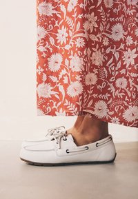 Hvide læder bådsko med sorte øjelets og snørebånd, kombineret med en rød maxinederdel med blomstermønster, der viser detaljerede hvide blomster.