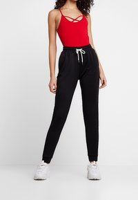 Corpetto rosso senza maniche con spalline e pantaloni jogger neri con vita elastica e lacci bianchi, abbinati a sneakers bianche.