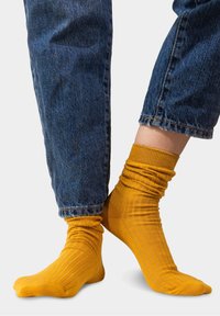 Żółte skarpetki o żebrowanym wzorze z luźnym krojem, noszone z niebieskimi dżinsami, ukazujące teksturę i dopasowanie wokół kostek.