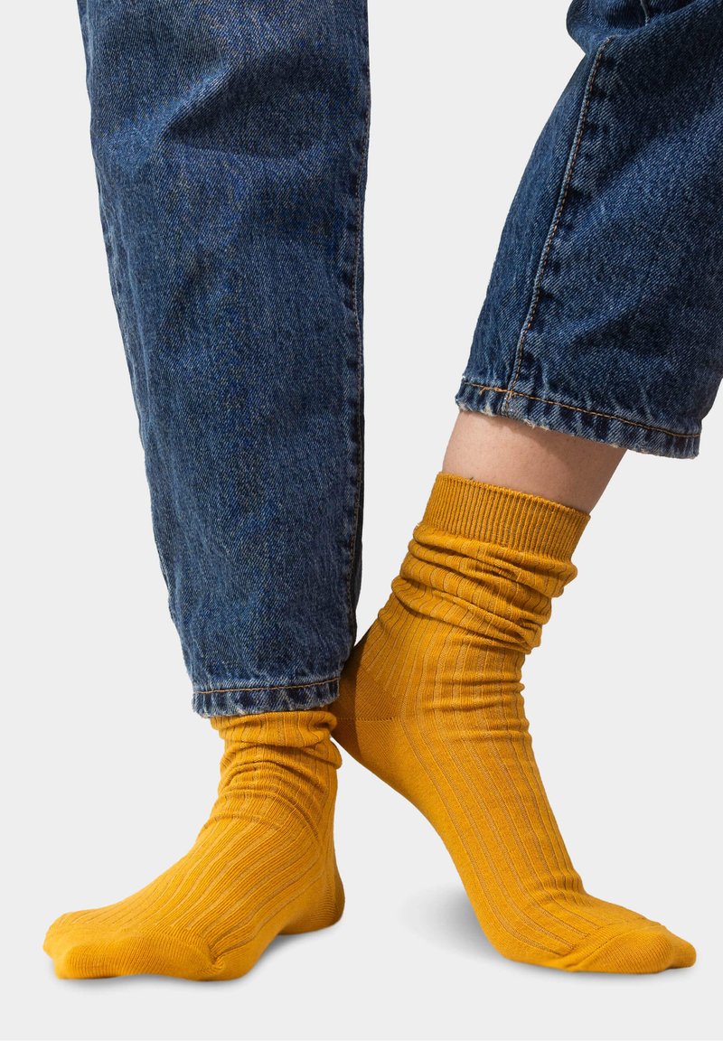 Żółte skarpetki o żebrowanym wzorze z luźnym krojem, noszone z niebieskimi dżinsami, ukazujące teksturę i dopasowanie wokół kostek.
