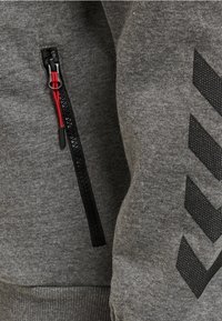 Gråt sweatshirtstof med en sidelukning med rød trækflig. Sort tekstureret chevronmønster på siden. Glat og blød tekstur.