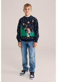 Mörkblå sweatshirt med renmotiv och träd samt prydnader, kombinerad med blå jeans och svarta sneakers. Mjukt tyg, avslappnad passform.