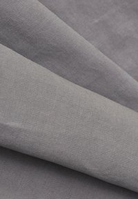 Tissu gris clair plié avec une texture côtelée horizontale fine, créant des ombres douces et des courbes lisses.