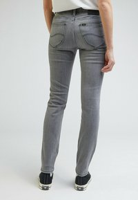 Jean en denim gris, coupe slim, taille mi-haute, cinq poches et coutures contrastées, assorti à des baskets en toile noire.